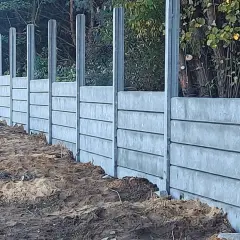 Nowe betonowe słupki ogrodzeniowe czekają na zalanie. Solidna konstrukcja wzdłuż leśnej ścieżki.