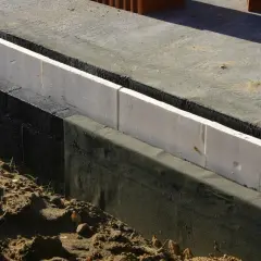Biały styrodur na fundamenty, izolacja przeciwwilgociowa i piasek na budowie.