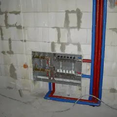 Instalacja hydrauliczna przed tynkami: widoczny rozdzielacz ogrzewania podłogowego i rury w ścianie z bloczków.