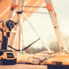 Wkrętarka i rękawice robocze leżą na desce. To niezbędne narzędzia na budowę, gotowe do pracy.