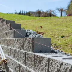 Budowa fundamentu pod murek oporowy. Betonowe bloki układane są warstwami, tworząc solidną konstrukcję na zboczu.