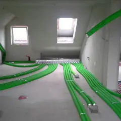 Instalacja rekuperacji w podłodze: zielone rury wentylacyjne rozchodzą się po pomieszczeniu, tworząc skomplikowaną sieć.
