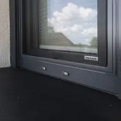 Montaż parapetów zewnętrznych do czoła okna, z widocznym logo DAKO. Ciemny parapet i szara rama okna.