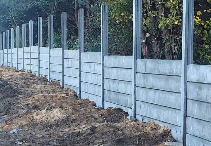 Nowe betonowe słupki ogrodzeniowe czekają na zalanie. Solidna konstrukcja wzdłuż leśnej ścieżki.