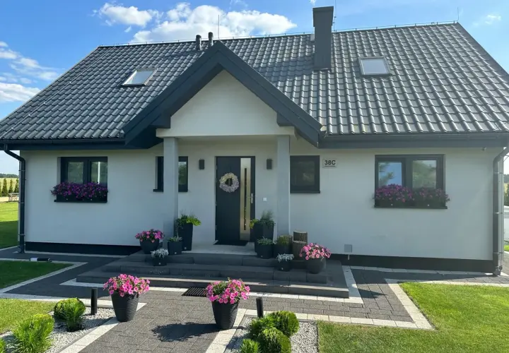 Uroczy dom Kamilek 100m2 z kwitnącymi petuniami w donicach i skrzynkach, zadbany ogród, nowoczesna elewacja.