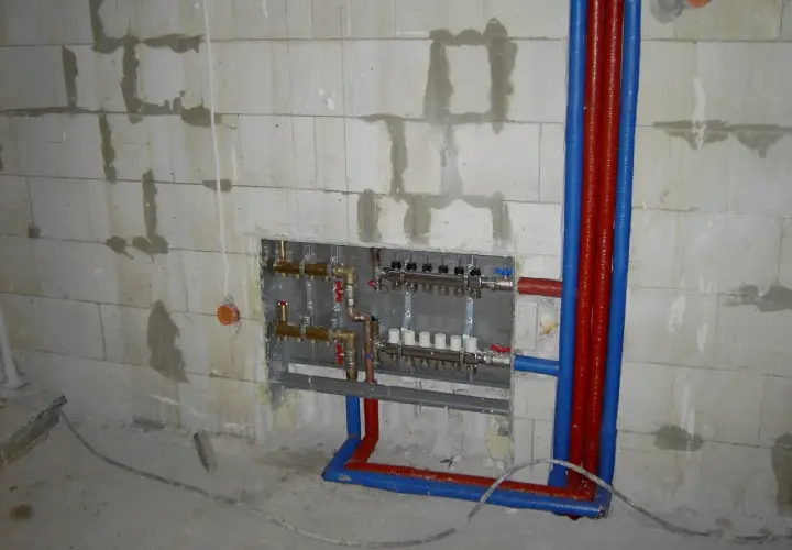 Instalacja hydrauliczna przed tynkami: widoczny rozdzielacz ogrzewania podłogowego i rury w ścianie z bloczków.