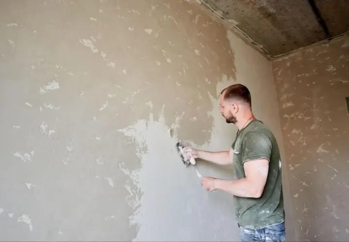 Mężczyzna szlifuje tynk cementowo-wapienny przed malowaniem, przygotowując ścianę do wykończenia.