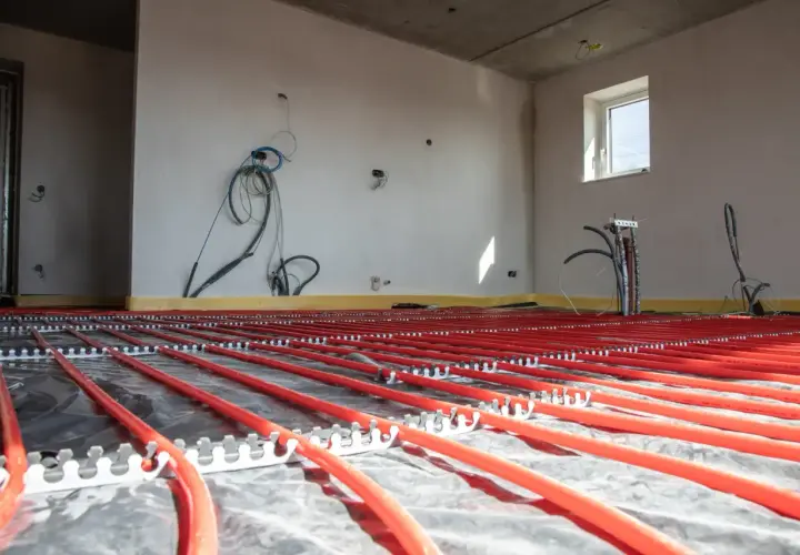 Instalacja podłogówki w garażu w trakcie budowy. Czerwone rurki systemu grzewczego ułożone na folii izolacyjnej.