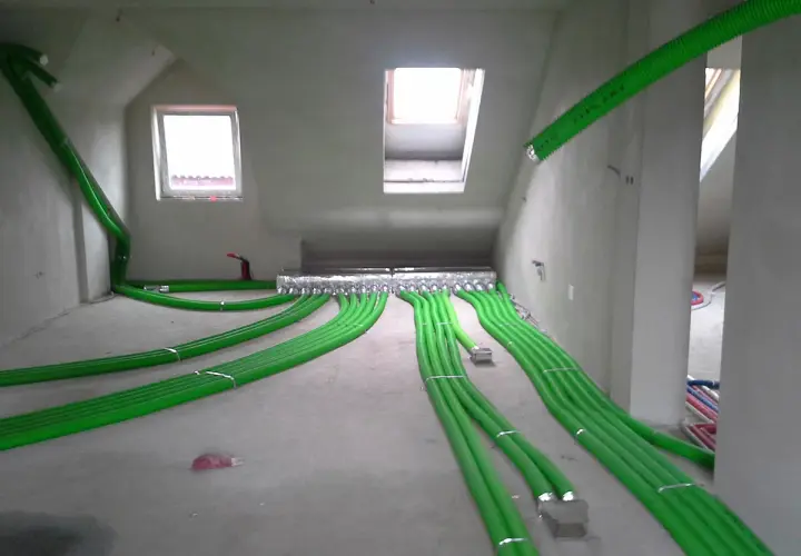 Instalacja rekuperacji w podłodze: zielone rury wentylacyjne rozchodzą się po pomieszczeniu, tworząc skomplikowaną sieć.