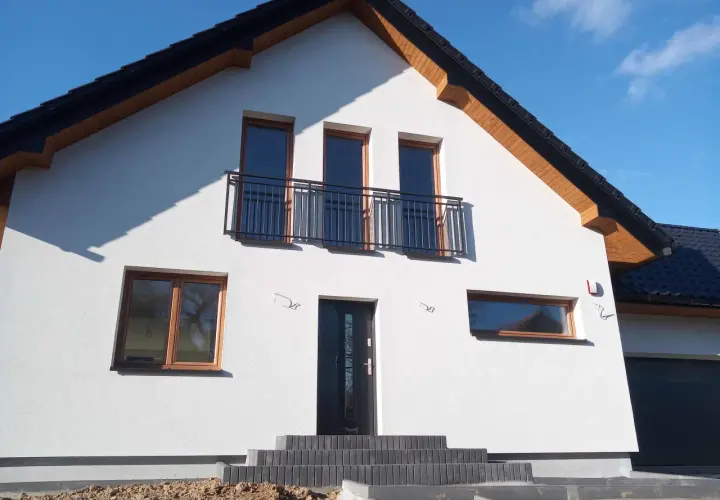 Nowy dom z białym tynkiem, antracytowym dachem i oknami w kolorze winchester.