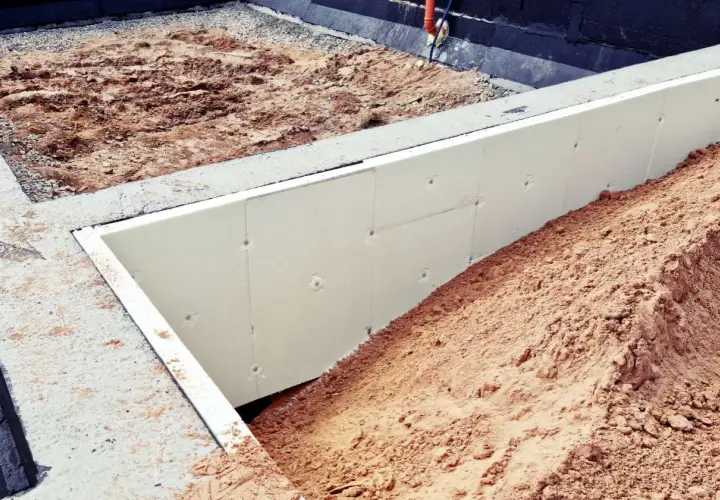 Płyty styropianowe na fundamenty chronią budynek przed zimnem. Widać je na placu budowy, otoczone ziemią.