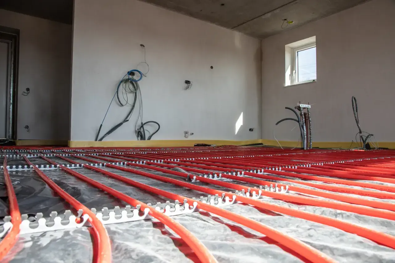Instalacja podłogówki w garażu w trakcie budowy. Czerwone rurki systemu grzewczego ułożone na folii izolacyjnej.