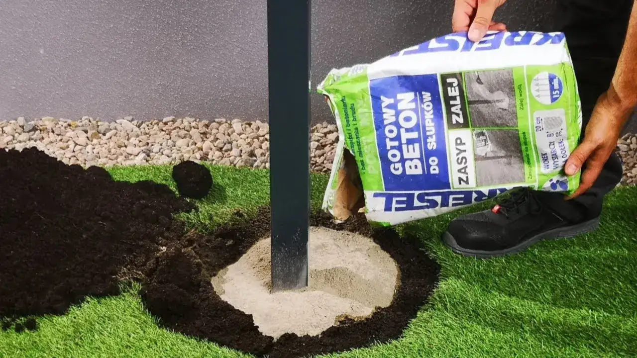 Gotowy beton do słupków ogrodzeniowych wsypywany do dołu wokół metalowego słupka.