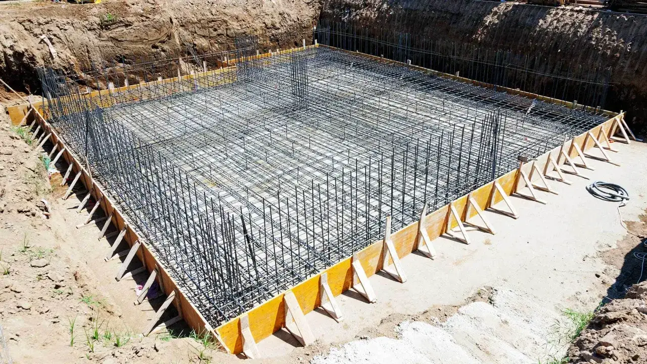 Wykop pod fundament z gęstą siatką zbrojeniową i drewnianym szalunkiem. Budowa solidnej podstawy dla przyszłego budynku.