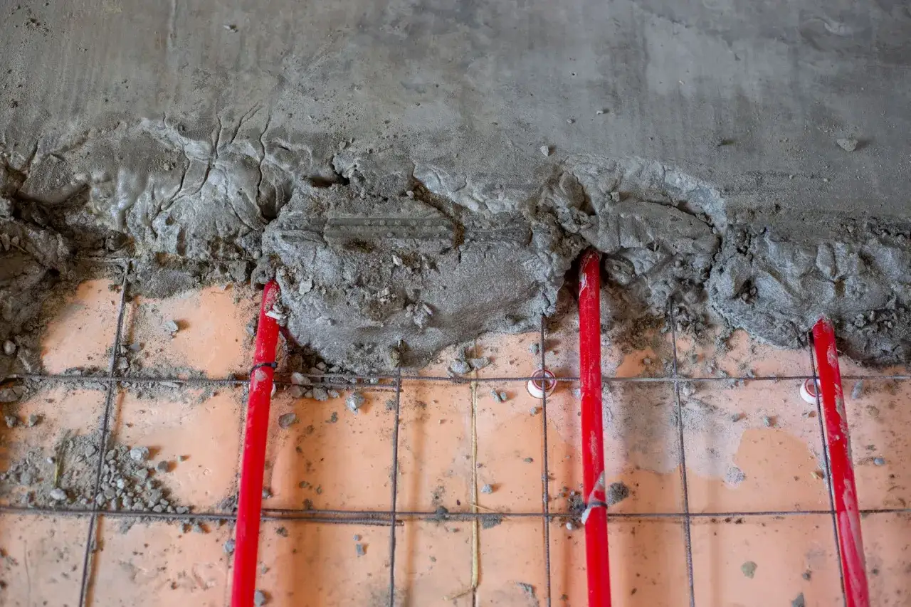 Grubość wylewki w garażu: czerwone rurki ogrzewania podłogowego wtopione w beton.